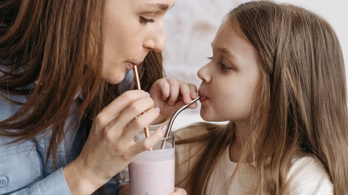 A mother and daughter sharing a strawberry milkshake indoors, depicting love and bonding.